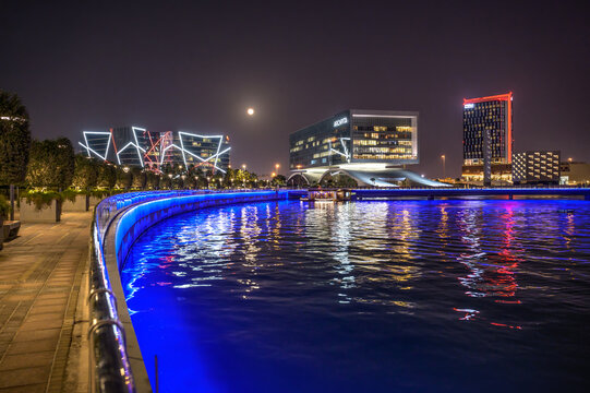 Manama, Bahrain - December 27, 2023 : Night view of Bahrain Bay in Manama featuring Arcapita, Hilton Garden Inn, and Al Baraka Tower with colorful waterfront lights and reflected in water.