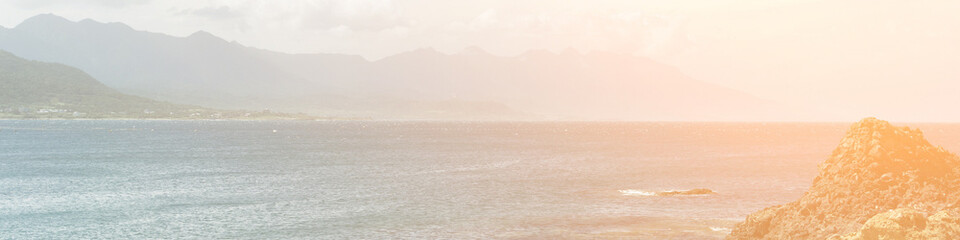 Peaceful coastal landscape with rocky shoreline, calm ocean waves, distant mountain range, and warm sunlight creating a serene natural outdoor atmosphere for travel projects.