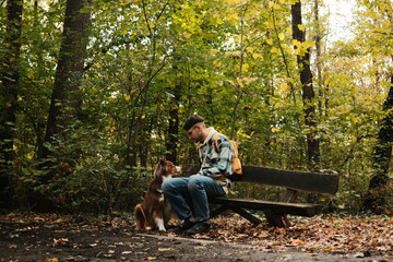Man with Australian Shepherd dog sitting on wooden bench in forest, sharing calm moment. Concept of friendship, nature, and relaxation with pet