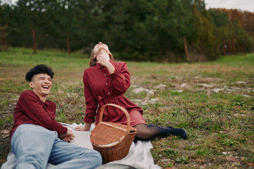 Candid outdoor picnic portrait of two friends laughing on a blanket by a grassy field, conveying warmth, authenticity and trustworthiness through natural expressions and relaxed pose.