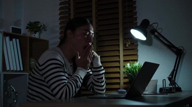 sleepy woman yawning while working with laptop at a night