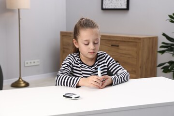 Naklejka premium Diabetes. Little girl checking blood sugar level with lancet pen at white table indoors