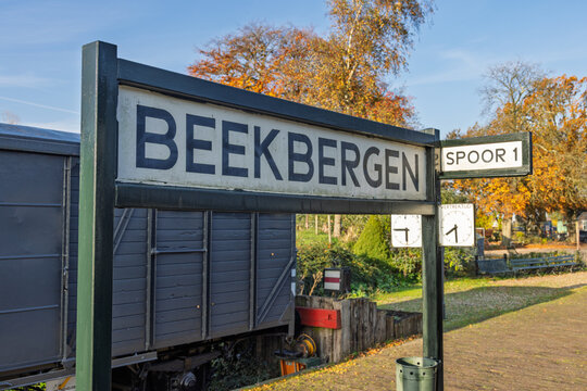 A wooden sign for "Beekbergen" and "Spoor 1" (Track 1) at the small heritage railway station, featuring an old wagon in the background.