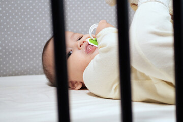 Baby sucking Pacifier looking on bed. portrait of cute newborn baby lying on bed with pacifier on...
