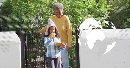 Smiling senior wearing mustard knit standing behind child at iron gate, child holding apple, basket