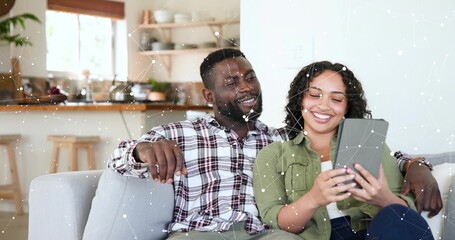 Sharing tablet, man in plaid shirt and woman in olive shirt sitting on couch in kitchen