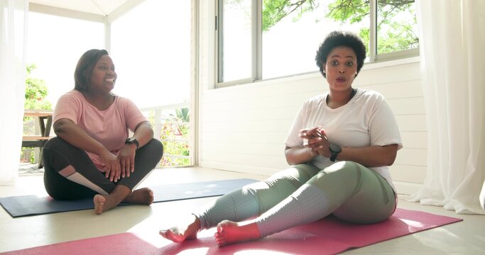 Gesturing woman in green leggings sitting on pink mat in sunroom with blue mat, wristwatch - Powered by Adobe