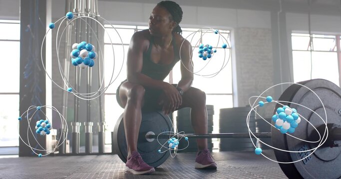 Sitting fit woman wearing sports bra and shorts, resting on loaded barbell in studio, atom overlays - Powered by Adobe