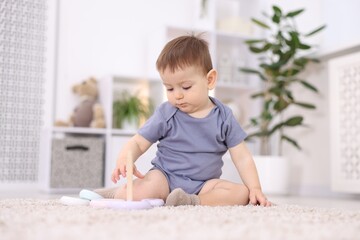 Fototapeta premium Cute little baby sitting and playing with toy on floor at home