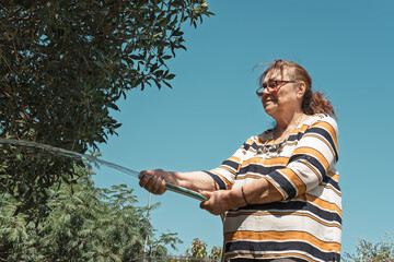 Senior woman watering plants in her home garden on a sunny day