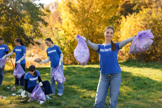 Group of happy volunteers with bags collecting trash in park