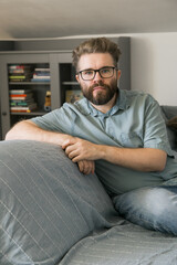Fototapeta premium Man sitting on couch in home living room. Representation of relaxation, thoughtfulness, and calm everyday moment in domestic environment.