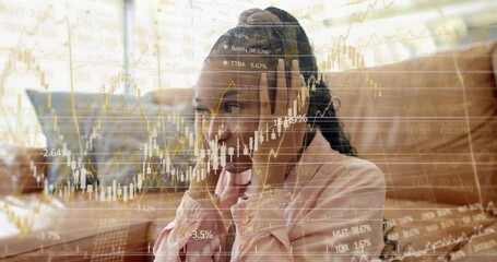 Woman on sofa pressing ears, taking offscreen item while faint stock charts overlay tracking stocks