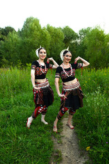 Fototapeta premium Two Indian dancers in fancy dance costumes outdoors against the backdrop of nature and forestTwo Indian dancers in fancy dance costumes outdoors against the backdrop of nature and forest