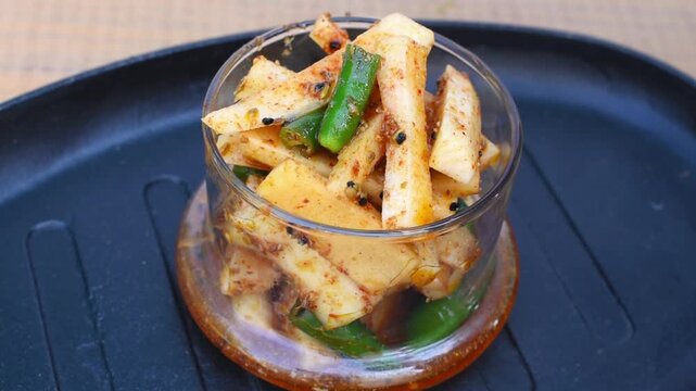 Pouring masala oil on Mooli Hari Mirch Achar that is Radish and Green Chili Pickle served in a glass jar placed on tray