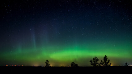 Night sky with a green aurora borealis over the forests of Western Finland