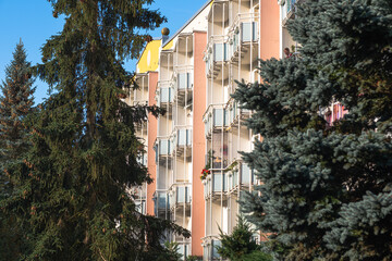 A multi-story building with red balconies and fir trees next to it. A German apartment building with balconies. Some balconies have flowers or parasols