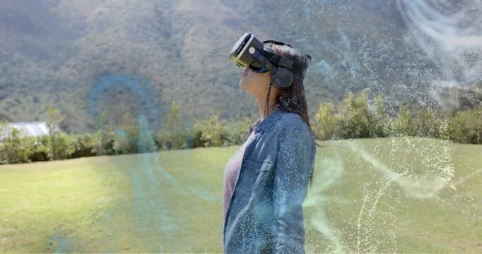 Teen using VR walking across lawn, pausing, looking up while blue overlays growing, exploring VR