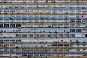 Full frame facade of a large residential or commercial building, densely packed with windows and numerous air conditioning units, showcasing urban living and density.