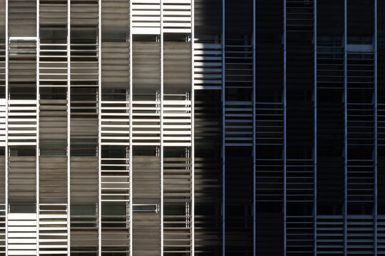 Striking view of a modern building facade with a clear division between bright sunlight and deep shadow, highlighting its repetitive grid pattern.