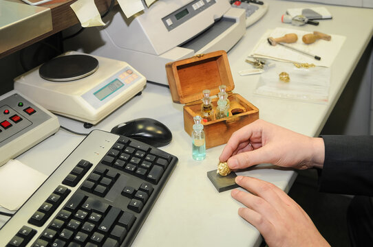Closeup of a person's hands checking the purity of a gold jewel on a table.