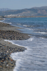 Pebble beach with gentle sea waves and mountains in the background