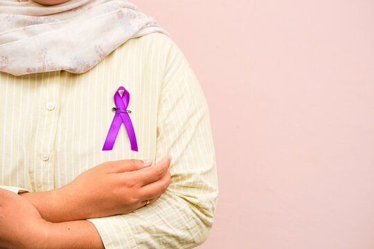 Pinned purple ribbon on woman wearing casual hijab against pink background, symbolizing health awareness, support, and solidarity. For design concept with copy space