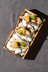 Elegant gourmet appetizer: crispy crackers topped with creamy filling, caviar, and vibrant green sauce, artfully arranged on white pebbles in a rustic wooden tray. Perfect for high-end food