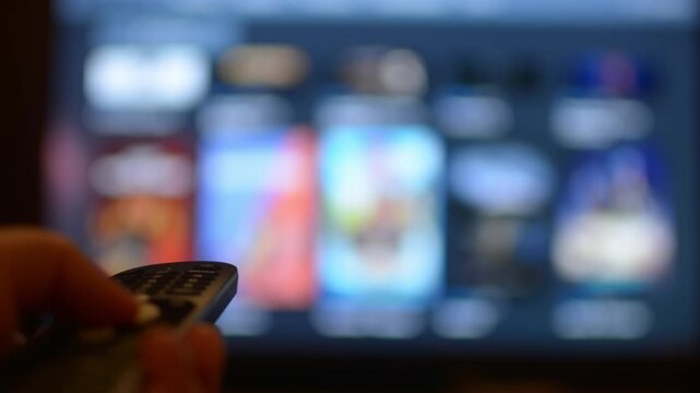 Person browses smart TV menu using remote control, switching between streaming services and selecting content to watch