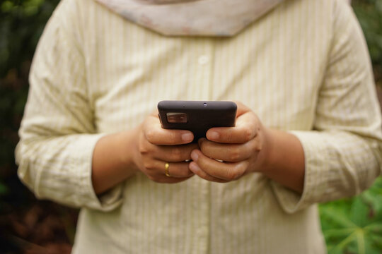Selective focus on woman typing on smartphone with both hands outdoors, representing social media, messaging, mobile activity, and digital lifestyle.