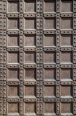 Old wooden door with square carved panels. Vintage texture of historic entrance. Antique architectural detail with geometric wood pattern. Medieval door design with decorative metal studs.
