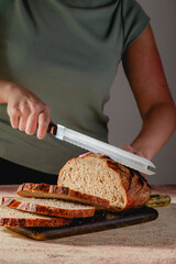 Woman Slicing Fresh Sourdough Bread on Dark Cutting Board
