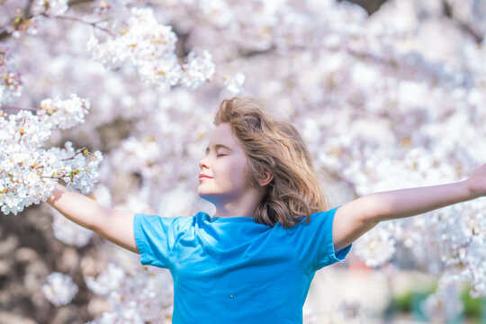 Peaceful kid with raised hands meditating, feeling calm near cherry blossom tree. Kid practice yoga and relaxed on spring nature. Kid closed eyes and feeds energy of nature, dreams. Spring blossom.