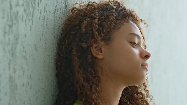Teenage Girl Leaning Against Green Wall In Profile With Blank Expression, Lost In Thought And Experiencing A Silent Emotional Moment