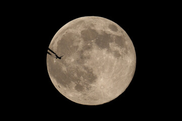 Fototapeta premium The moon and an airplane in the night sky. The plane is flying across the moon, against a black background.