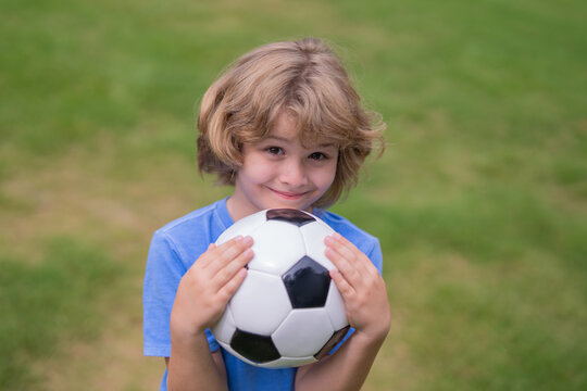 A happy kid holds a soccer ball. Kid football player portrait. Child shows soccer ball. Little soccer player enjoys sports outdoors. Boy playing football. The boy dreams of soccer success.
