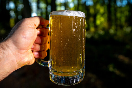 Golden craft beer. Fresh lager beer with foam in beer glass mug. Hand pouring amber ale beer in nature. - Powered by Adobe