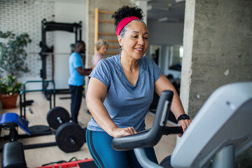 Mature woman smiling while cycling on exercise bike at gym