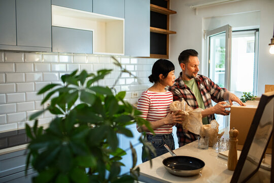 Adult couple happily unpacking boxes in bright home kitchen