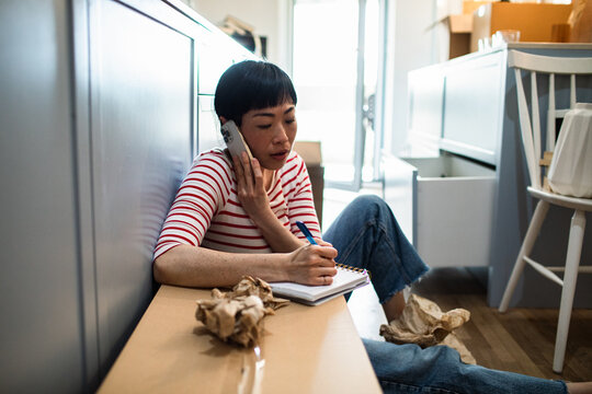 Adult woman stressed on phone taking notes on kitchen floor