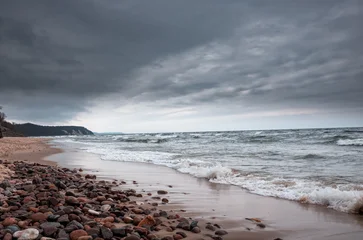A moody coastal scene featuring a pebbled shoreline, crashing waves, and a dramatic stormy sky. The dark clouds mirror the turbulent sea, creating a sense of solitude and natural power © splendens