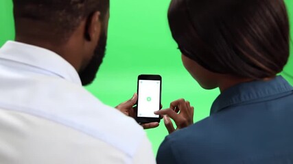 Two diverse individuals a man and a woman are seen from behind intently focused on a smartphone screen displaying a green recycling icon set against a vibrant green screen background suggesting a foc. - Powered by Adobe