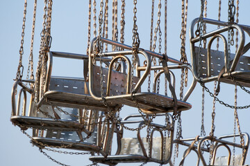 A close-up of a children's playground swing hanging from a chain against a blue sky background