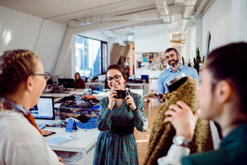 Young adult woman smiling while photographing clothing in creative office