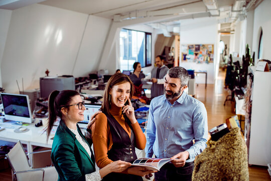 Adult coworkers laughing while reviewing catalog in design studio