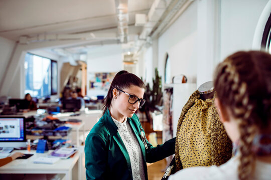 Adult woman fashion designer inspecting dress on mannequin in studio, focused