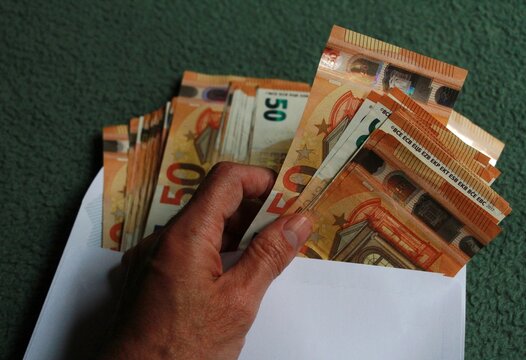Mano con dinero y plata en billetes de cincuenta euros en sobre blanco con pasta en money cash