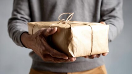 Close up view of male hands holding a gift box wrapped in recycled brown paper and tied with twine, presenting a sustainable and thoughtful present for any special occasion or holiday