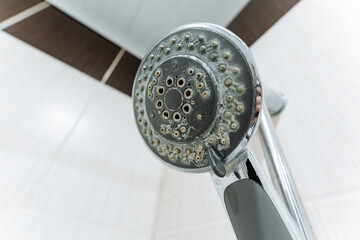 Cleaning limescale from shower fixtures, Homeowner removing mineral deposits from shower heads, Closeup of clogged shower nozzle with mineral buildup and homeowner performing cleaning tasks