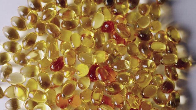 Top-down, close-up video of golden softgel capsules, like vitamin or fish oil supplements, slowly rotating on a turntable on white background showing concepts of healthcare, medicine, and nutrition.